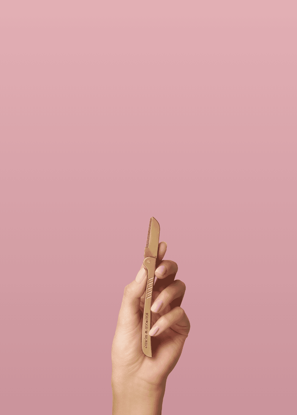 Hand holding a gold eyebrow razor against a pink background